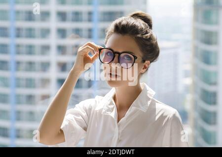 Junge Geschäftsfrau, die neben dem großen Fenster steht. Büro im modernen Gebäude der Großstadt Stockfoto