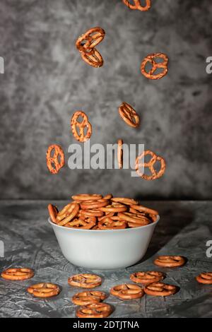 Levitation von Lebensmitteln. Kleine Plätzchen in Form von Brezeln, die in eine Tonschale fallen, Holzhintergrund. Stockfoto