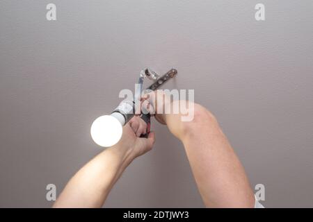 Elektriker hängt einen Kronleuchter an der Decke in einer Wohnung. Verbesserung und Reparatur der Räumlichkeiten. Beschäftigung. Stockfoto