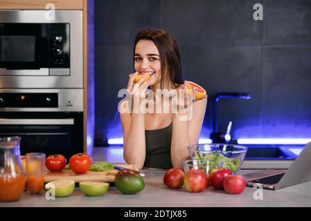 Junge schöne Frau beißt Grapefruit oder Orange am Morgen in der Küche. Stockfoto