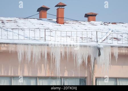 Große Eiszapfen hängen vom Dach des Gebäudes in Winter und es gibt Schnee auf dem Dach Stockfoto