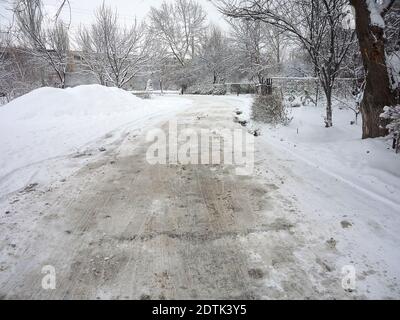 Straße durch die Bäume im Winter ist mit einem bedeckt Dicke Schicht schmutzigen losen Schnees Stockfoto