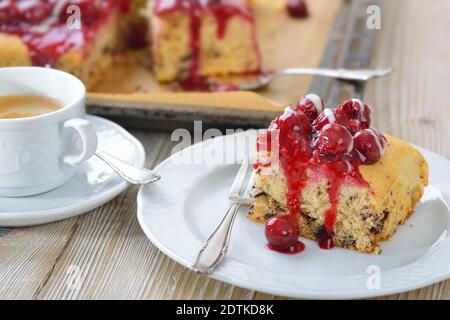 Süßer Stracciatella Kuchen mit rotem Fruchtgelee, Kirschen und Vanillesauce bedeckt, serviert mit Kaffee Crema Stockfoto