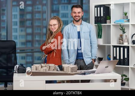 Professionelle Architektin steht mit einer hübschen Kollegin mit Dreadlocks im Designstudio zurück an den Rücken. Stockfoto