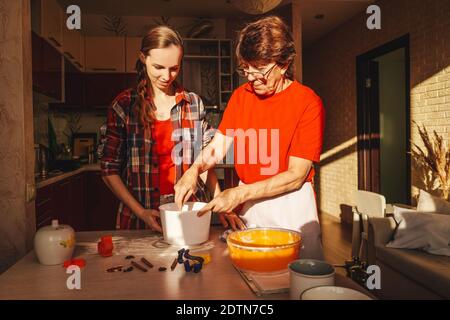 Junge Frau und ältere Mutter kochen Kekse in roten Kleidern. Stockfoto
