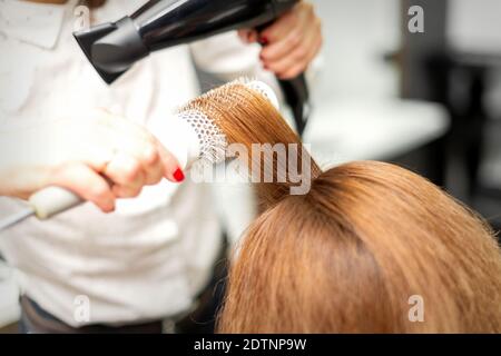 Nahaufnahme von Friseur Trocknen lange rote Haare mit einem Haartrockner und Rundbürste in einem Schönheitssalon Stockfoto