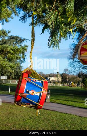 Festlich dekorierte Trommel hängt an einem Baumzweig in einem Park an einem hellen Tag mit einem malerischen Blick auf die Gebäude in Trentham Gardens, Stoke on Trent Stockfoto