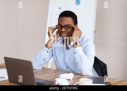 Erschöpfter schwarzer Manager, der Kopfschmerzen hat, während er im Büro arbeitet Stockfoto