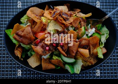 Fattoush (libanesischer Salat) Nahaufnahme Bild in einem schwarzen Teller . Es wird mit Gemüse und knusprigem geröstetem Fladenbrot zubereitet, das das Dressing aufsaugt Stockfoto