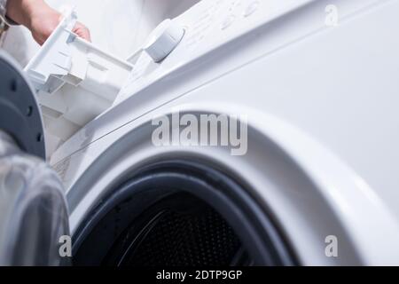 Waschpulver in eine Waschmaschine geben. Wäscheservice Tag zu Hause. Stockfoto