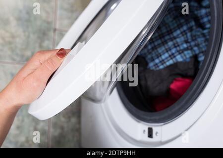 Frau die Hand öffnen Waschmaschine, um andere Kleidung zu laden Stockfoto