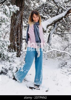 Fröhliche Mode junge Frau, die im Winter zwischen verschneiten Bäumen steht Wald und genießen ersten Schnee Stockfoto