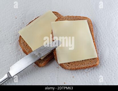 Blick von oben auf ein Buttermesser auf zwei Scheiben Weizenbrot mit Margarine und Käse auf Papierhandtüchern, die mit natürlichem Licht beleuchtet sind. Stockfoto