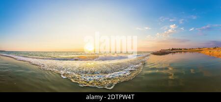 Abstraktes Panorama des Sonnenuntergangs Himmel über Meer ohne Wolken und sanfte Welle im Vordergrund. Eine goldorange Sonne untergeht mit ihrer Spiegelung zitternd. Der Stockfoto