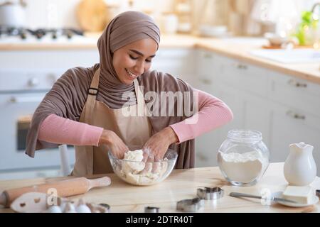 Backkonzept. Lächelnde Muslimische Frau In Hijab Knetteig In Der Küche Stockfoto