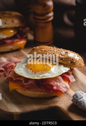 Frühstückssandwich mit Spiegelei, Speck und Käse auf einem Holzbrett Stockfoto