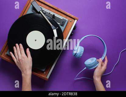 DJ-Konzept. Weibliche Hände verwendet Vinyl-Player und hält die Kopfhörer in der Hand vor lila Hintergrund. Retro-Style. Popkultur. Draufsicht Stockfoto