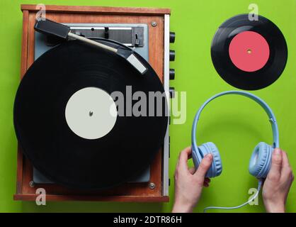 Weibliche Hände halten Kopfhörer vor dem Hintergrund von Retro-Vinyl-Schallplattenspieler mit Vinyl-Schallplatten auf grünem Hintergrund. Retro-Style. 80er. Draufsicht Stockfoto