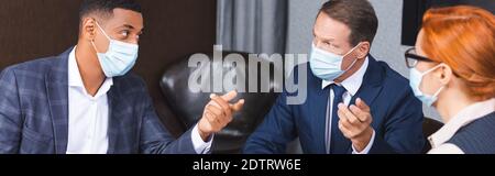 Multikulturelle Geschäftsleute in medizinischen Masken während der Diskussion in der Nähe weibliche Kollegin im Sitzungssaal, Banner Stockfoto