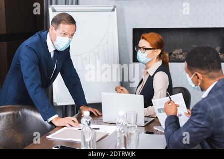 Geschäftsmann in medizinische Maske Blick auf afroamerikanischen Kollegen während Lehnen Sie sich am Arbeitsplatz im Tagungsraum Stockfoto
