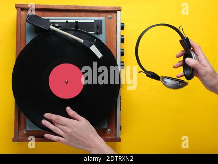 Retro-Stil, DJ spielt Vinyl-Plattenspieler und hält Kopfhörer in der Hand, Minimalismus, Draufsicht auf gelbem Hintergrund Stockfoto