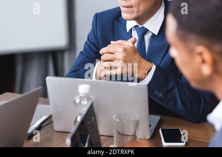 Führungskräfte mit geballten Händen, die mit digitalen Geräten am Arbeitsplatz sitzen Fast verschwommener afroamerikanischer Geschäftsmann im Vordergrund Stockfoto