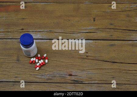 Topf mit Medikamentenkapseln, weißer Topf mit blauem Deckel, blaue und weiße Kapseln auf Holzhintergrund, Draufsicht, Kopierraum Stockfoto