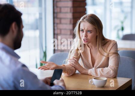 Wütend junge Dame streiten mit ihrem Freund stecken in Smartphone, unglücklich über Vernachlässigung und Mangel an Kommunikation Stockfoto