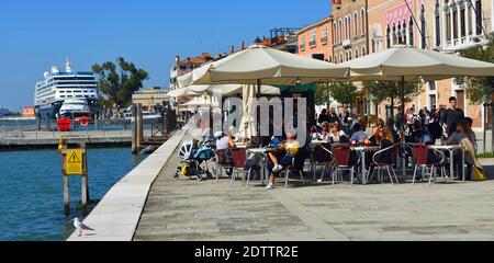 Cafe an der venezianischen Lagune mit Kreuzfahrtschiff im Hintergrund. Stockfoto