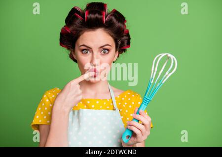 Foto von schönen niedlichen jungen Mädchen Roller Frisur Lippen lecken Finger Tasting Teig backen Keks halten Kunststoff Schneebesen starren geschockt Tragen Sie gepunktete Schürzenhemd Stockfoto