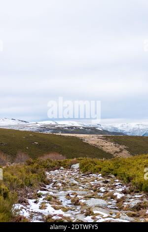 Vertikales Panoramabild eines mit Schnee bedeckten Steinweges Und Eis in der Vegetation, die einige verschneite Berge durchquert In Europa Stockfoto