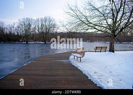 Schneebedeckte Holzbänke mit Blick auf dünnes Eis in einem kleinen See im Turkey Swamp Park, New Jersey, USA -01 Stockfoto