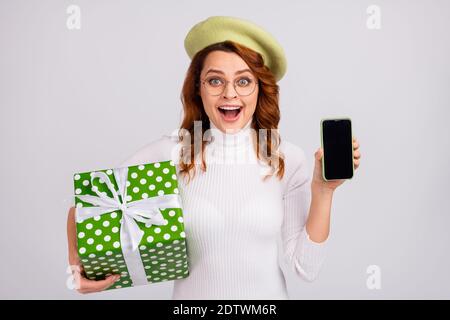 Portrait von schönen fröhlich wellig-haarige Mädchen in den Händen halten geschenkbox Zeigt das Gerät isoliert auf hellweißem grauem Hintergrund an Stockfoto