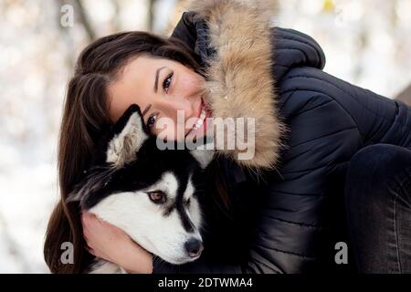 Schöne junge Frau umarmt weibliche Husky Hund im kalten Winter Schneebedeckter Tag Stockfoto