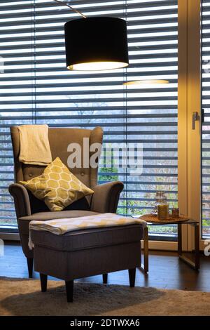 Modernes Wohnzimmer mit einem Lesesessel unter einem stilvollen Stehlampe und jalousien Stockfoto
