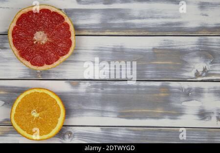 Draufsicht auf zwei vereinzelte Obsthälften, rot-reife Grapefruit und Orange, auf weißem Naturholztisch mit Platz für Text Stockfoto