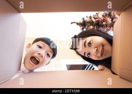 Das überraschte Kind und die Mutter beim Auspacken, beim Öffnen des Kartons und beim Blick nach innen. Auspacken Innenansicht, asiatische Familie. Stockfoto