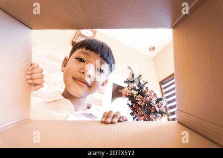 Das glückliche Kind Auspacken, Öffnen der Karton-Box und Blick nach innen. Das kleine asiatische Kind Unboxing Geschenk Innenansicht. Stockfoto