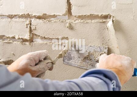 Professional Builder moulding decorative tile on wall from gips plaster . worker removing tape under plaster to imitate decorative brick on wall Stockfoto