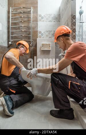 Die Arbeiter installieren eine an der Wand aufgehängte Toilette. Stockfoto