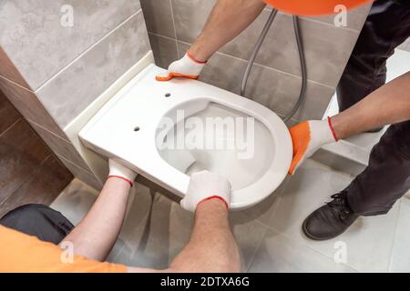 Die Arbeiter installieren eine an der Wand aufgehängte Toilette. Stockfoto