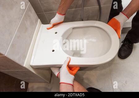 Die Arbeiter installieren eine an der Wand aufgehängte Toilette. Stockfoto