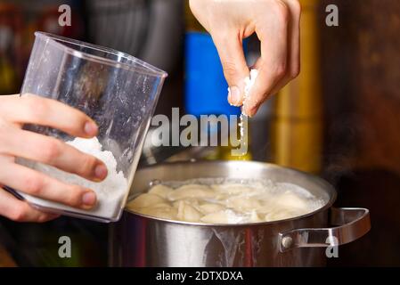 Salz in einen Topf mit kochenden Knödeln geben. Gekochte Knödel in einer Pfanne Stockfoto