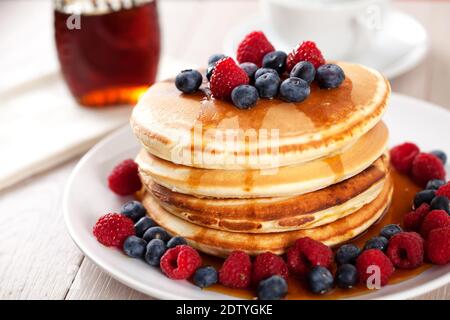 Pfannkuchen mit Beeren und Ahornsirup auf einem Teller. Stockfoto