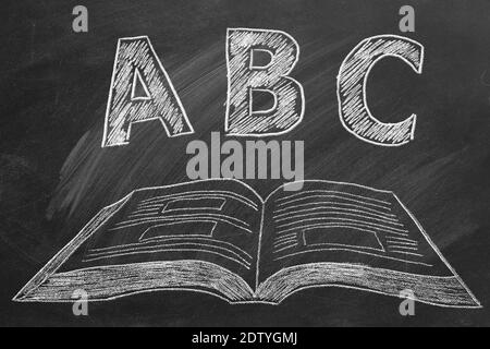 ABC-Briefe mit offenem Buch in Kreide auf Tafel. Grundschule. Stockfoto