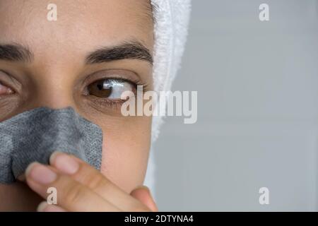 Eine Frau klebt einen Reinigungsstreifen auf ihre Nase. Schwarze Punkte auf der Nase. Mädchen ohne Make-up im Badezimmer. Hautpflege, Problemhaut, Reinigung. Natürlich Stockfoto