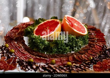 Vorspeise mit Fleisch. Frisch geschnittenes Obst auf dem Festtisch. Wurst und Grapefruit schneiden. Stockfoto