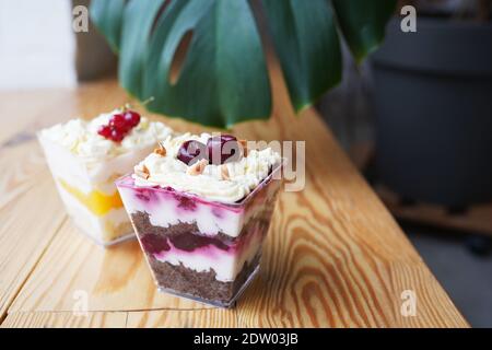 Desserts Heidelbeeren mit Sahne und Schokolade Keks und Pfirsich mit Sahne und Vanille Keks verziert Beeren in quadratischen Gläsern auf Holztisch. Stockfoto