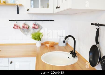 Blick auf weiße Küche im skandinavischen Stil, Küchendetails, Baumpflanze auf Holztisch, weiße Keramik Backstein Wand Hintergrund Stockfoto