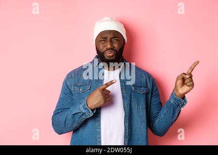 Enttäuschter und skeptischer afroamerikanischer Typ, der sich beschwert, vor Ekel, Stirnrunzeln und Grimassen vor Unzufriedenheit, Finger nach rechts zeigend Stockfoto